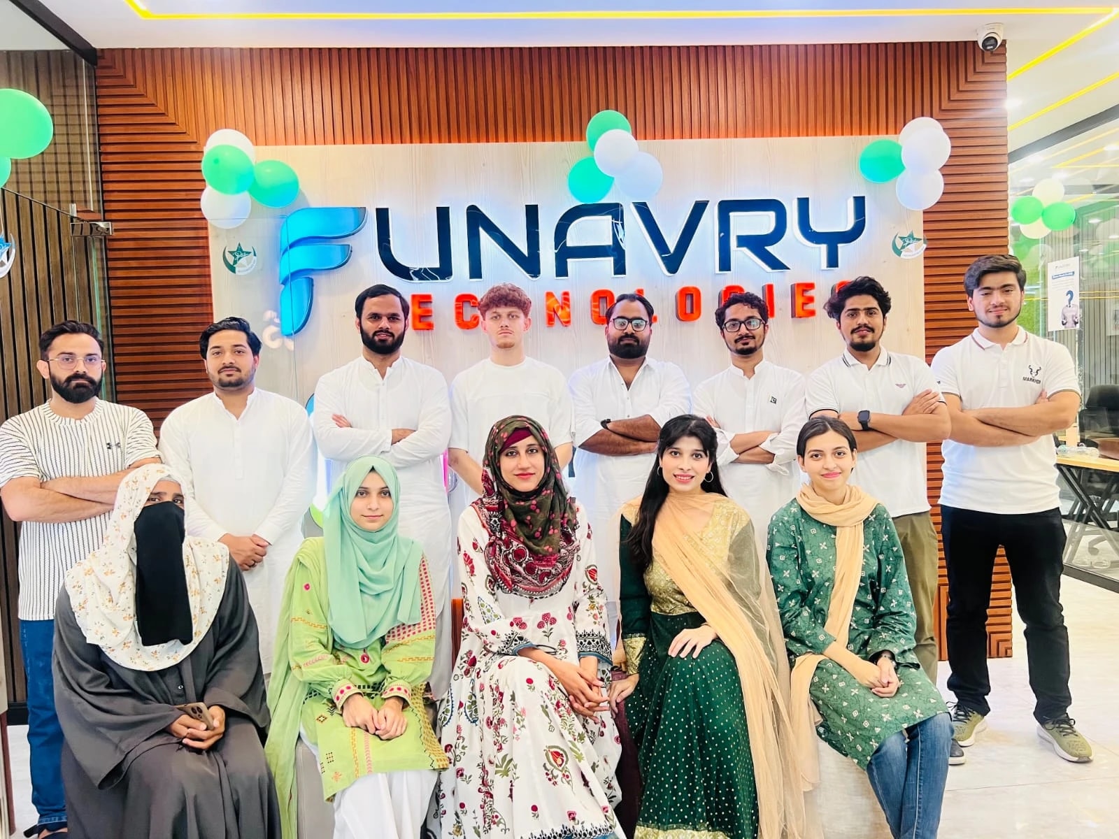 The team gathered in front of the illuminated Funavry Technologies sign at the office, under green and white balloons