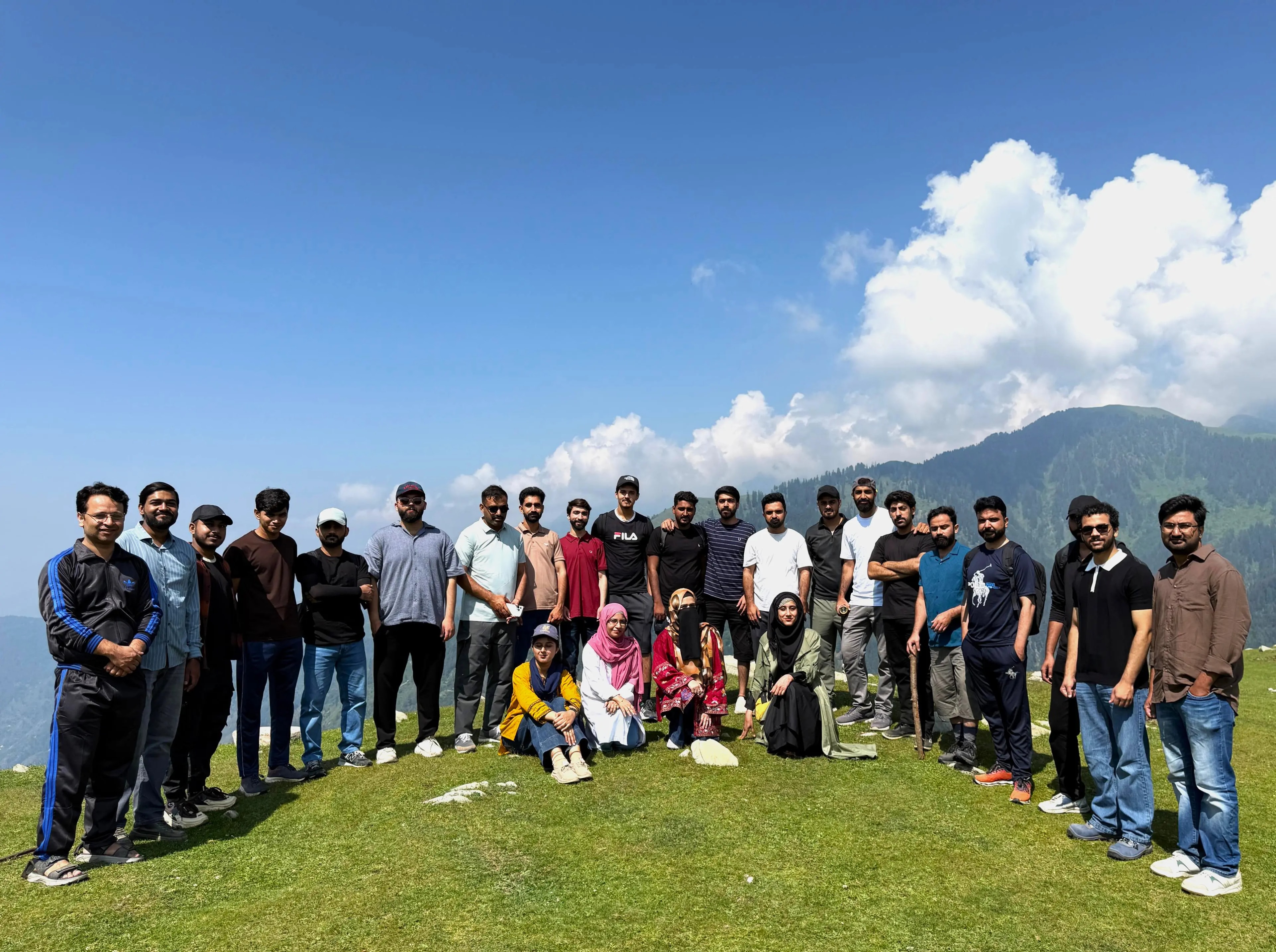 The team on a grassy mountaintop under a blue sky and white clouds on a company trip